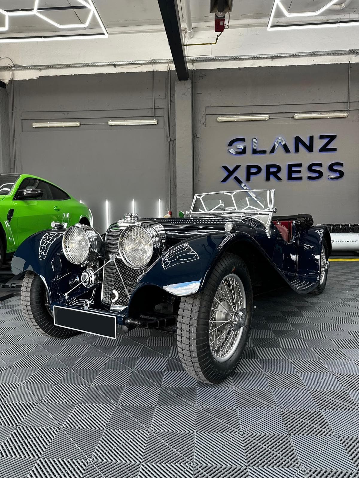 Dunkelblauer Jaguar-Roadster mit Speichenrädern vor dem GlanzXpress-Schriftzug in unserer Halle in Oranienburg